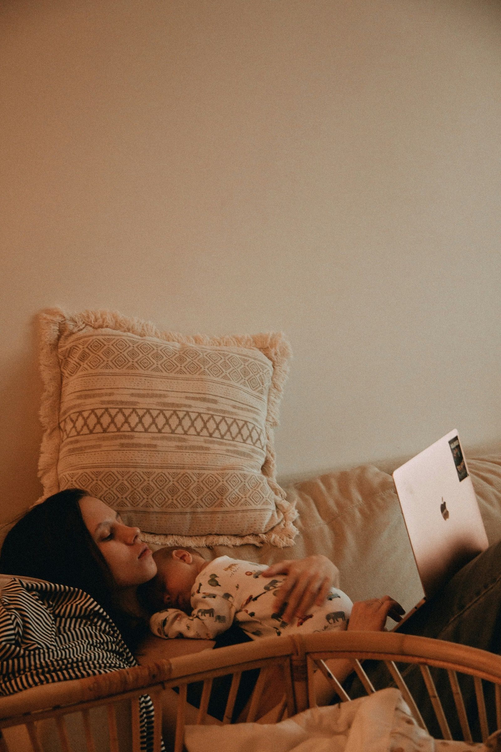 Retailer managing her online store on a laptop at home while a baby sleeps on her chest